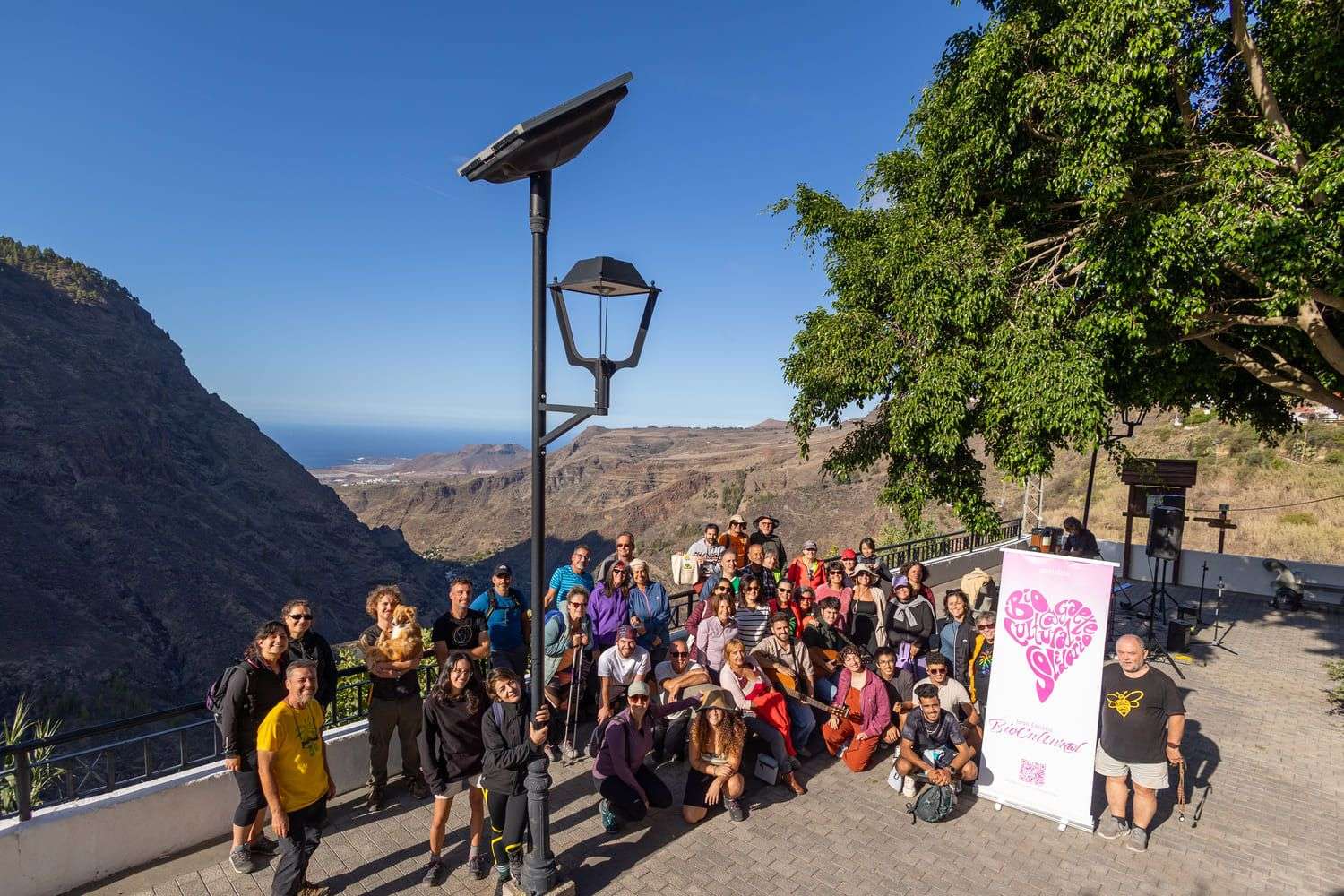Entre montañas y tradiciones: el legado cultural de El Hornillo. La asociación Bioagaete Cultural Solidario volvió a reunir naturaleza, memoria y comunidad en una nueva edición de sus caminatas interpretativas, el pasado sábado. Bajo el título “Entre montañas y tradiciones. El legado cultural de El Hornillo”, una treintena de participantes a pie y otros tanto en transporte, emprendieron un recorrido circular que partió desde San Pedro para adentrarse en los parajes de El Sao y  El Hornillo, en el municipio de Agaete.  La jornada transcurrió por antiguos caminos reales, senderos que durante siglos conectaron a los vecinos de El Valle y que hoy se recuperan como recurso educativo y patrimonial. En cada tramo, el grupo descubrió la riqueza botánica y faunística del entorno, así como la profunda relación que el territorio mantiene con el agua, elemento importante en la configuración cultural de El Valle de Agaete.  Las paradas interpretativas estuvieron guiadas por jóvenes especialistas de la asociación, quienes aportaron contexto histórico y ambiental. A este recorrido se sumó la intervención especial de Manuel González Medina, vecino de El Sao y propietario de uno de los últimos molinos de agua de la zona. Su testimonio permitió conocer historias que no se encuentran en los libros, cargadas de vivencias y saberes de un tiempo en que el agua era el corazón que marcaba el ritmo de la vida y del molino, que permitía llevar a las casas el preciado gofio para sustento de las familias de la comarca. Manuel permitió comprender de primera mano cómo era la gestión tradicional del agua, un conocimiento cada vez más escaso y de enorme valor etnográfico.  La jornada culminó en la plaza de El Hornillo, convertida por unas horas en escenario cultural y donde la tarde se transformó en un pequeño festival de talento local. Allí, bajo el cielo abierto y con el pinar de Tamadaba como telón de fondo, resonaron las voces de Salomé Moreno, Juan Fernando Quesada Ruiz y Juan Carlos Álamo del Rosario, representantes de una nueva generación musical que reivindica su territorio a través de la creación artística. Sus canciones, jóvenes pero profundas, llenaron el entorno de una energía renovadora, como si la música tejiera un puente entre el pasado y el futuro del Hornillo. El proyecto cuenta con la financiación del Instituto del Patrimonio Mundial y la Reserva de la Biosfera de Gran Canaria, dependiente del Cabildo de Gran Canaria, entidad dedicada a la protección, promoción y puesta en valor del Paisaje Cultural de Risco Caído y las Montañas Sagradas de Gran Canaria. Con iniciativas como esta, Bioagaete Cultural Solidario continúa su apuesta por resignificar el paisaje, conectar generaciones y promover un modelo de desarrollo sostenible  arraigado en la identidad insular. La actividad se enmarca en su línea de divulgación y dinamización rural, ofreciendo experiencias que permiten comprender la riqueza natural, histórica y etnográfica del territorio. Además, contribuye a mantener vivo el patrimonio de las Montañas Sagradas de Gran Canaria y a visibilizar el riesgo de despoblación que afecta a núcleos como El Hornillo, destacando el turismo sostenible como herramienta para la revitalización social y económica.